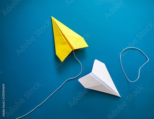 two paper airplanes one white and one yellow connected by a white line on blue background symbolizing change in direction and innovation