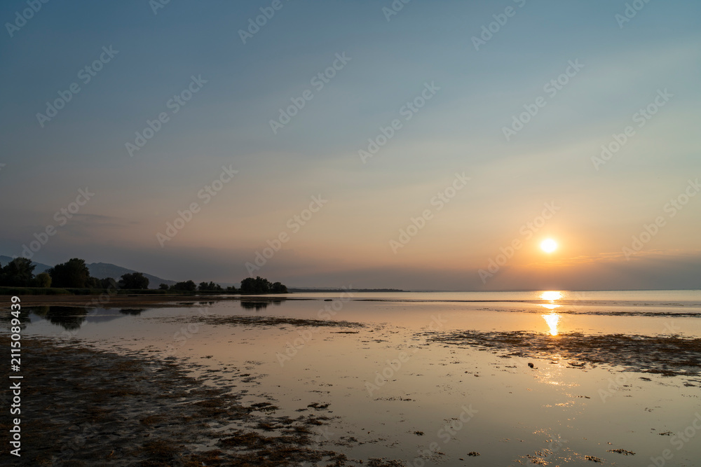 Obraz premium A serene golden sunset casting glowing reflections over the calm, shallow waters of Lake Constance as seen from the scenic Rohrspitz shore in Vorarlberg, Austria.