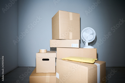 Close up of stacked cardboard boxes, padded mailer, tape roll, desk fan suggesting packing, shipping, moving, storage. Ideal for e commerce, delivery, relocation, logistics marketing