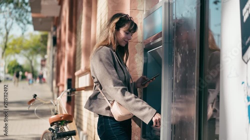 Video of beautiful woman withdrawing cash from an ATM using her smartphone in the city.