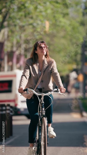 Video of smiling woman riding a bicycle in the bike lane through the city.