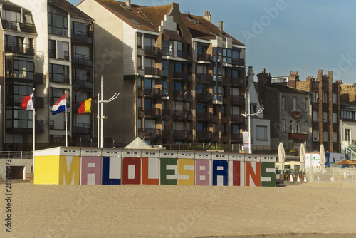 Фотография The Malo‑les‑Bains beach opens toward a row of tall seaside buildings, with bright letters and flags marking the lively Dunkirk shore