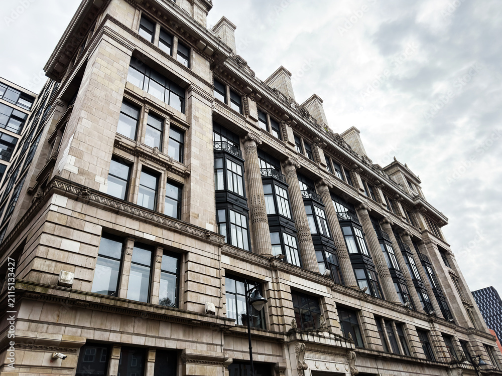 Obraz premium Historic stone office building with classical columns and large windows in Manchester, UK, urban commercial architecture under an overcast sky