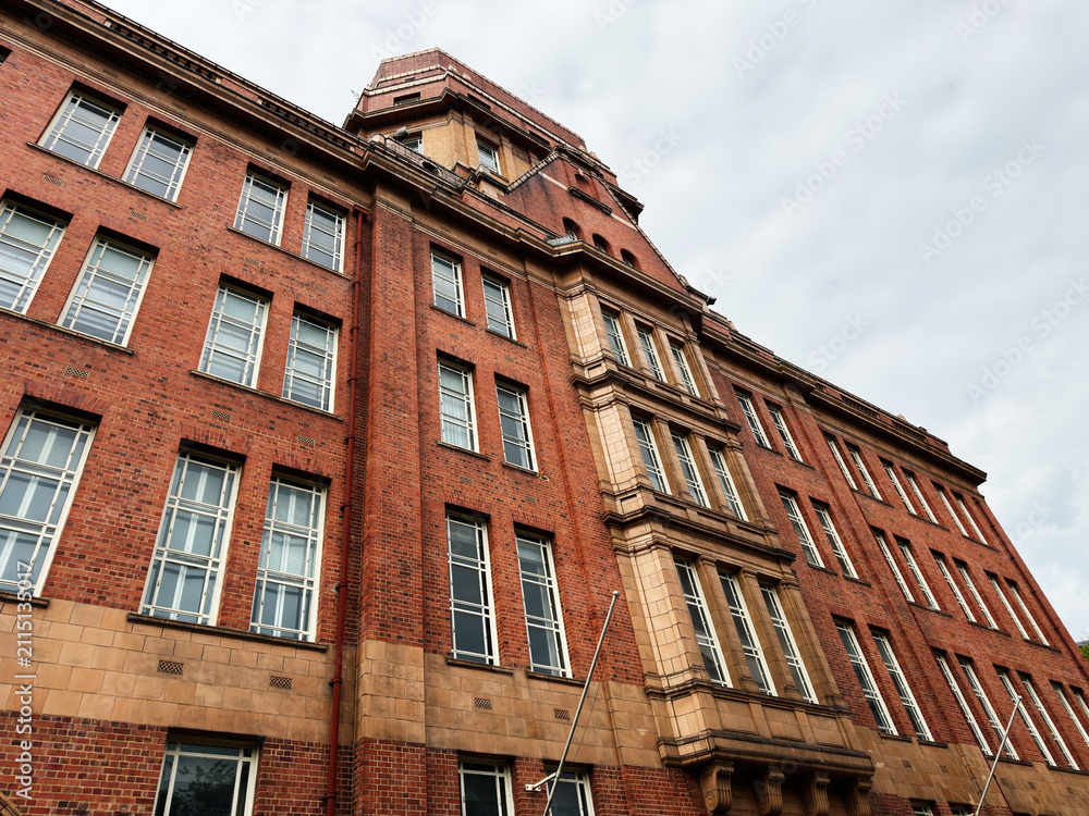 Obraz premium Historic red brick building facade and architecture with tower in Manchester, UK showing classic urban exterior and rows of windows