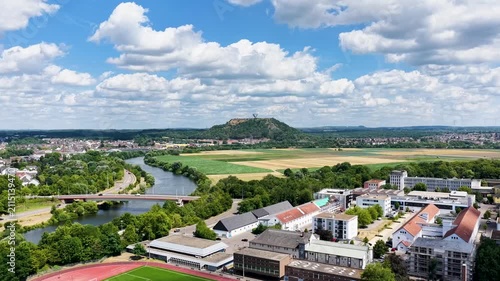 Vogelperspektive auf Saarlouis mit der vorbeifließenden Saar, einer markanten Straßenbrücke, dichter grüner Vegetation und der Stadtlandschaft unter blauem Wolkenhimmel.