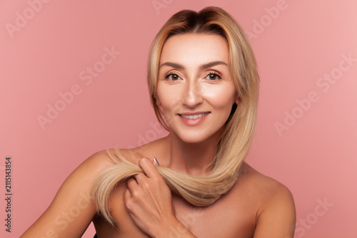 Cheerful woman showing her silky and strong hair strand for haircare products and shine demonstration isolated on pink background