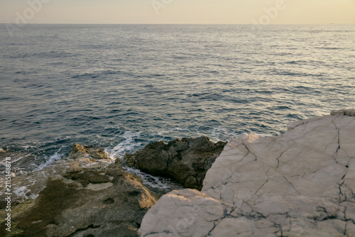 Canvas Print Calm sea water washing against rocky white limestone cliff shoreline at sunset