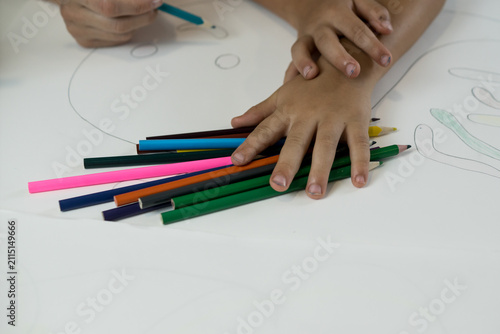 Bild auf Leinwand Close-up of a left-handed child placing their hand over a pile of colorful pencils while drawing on paper with guidance