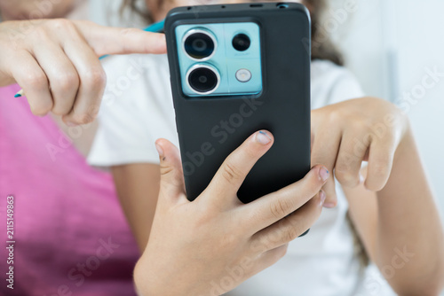 Obraz na plátně Detailed view of a left-handed child holding a smartphone while a parent assists with online educational content
