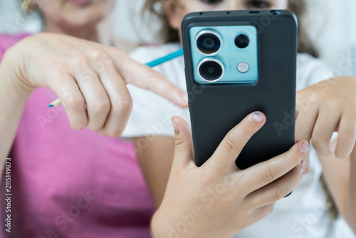 Close-up shot of a left-handed child holding a modern smartphone while a parent points toward the screen during a study session.