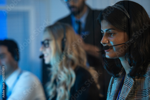 Indain call center agent or dispatcher in a headset  working urgently in a corporate operations room with colleagues. IT support  customer service  sales agent  project admin and telemarketing