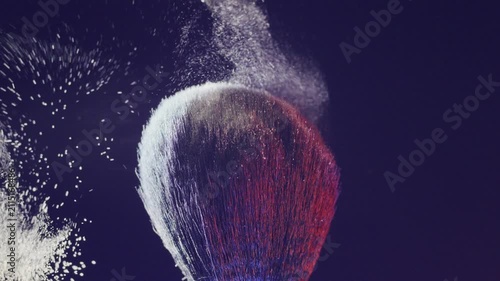 Closeup of brush with colorful powder release. Detailed shot of makeup brush releasing vibrant pigment against dramatic dark backdrop for beauty advertisement