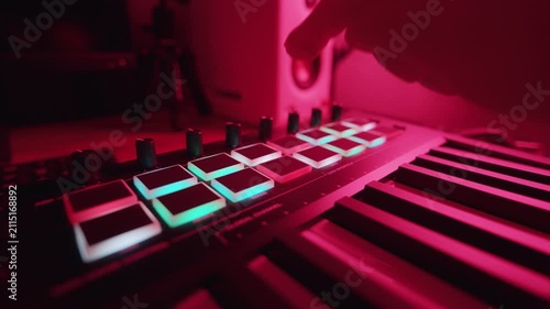 A person is using a music keyboard with colored lights in a home studio at night
