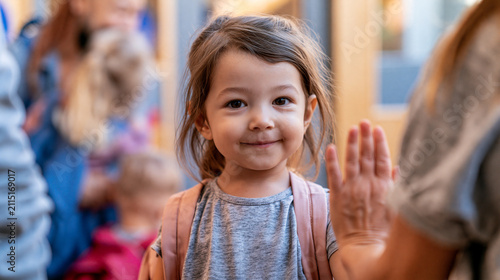 Young child calmly saying goodbye to a parent at preschool, turning toward a teacher in an authentic morning separation moment