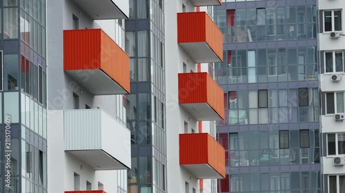 Contemporary facade featuring stacked terraces and glass panels. Overcast lighting accentuates architectural features and vibrant color contrasts on building