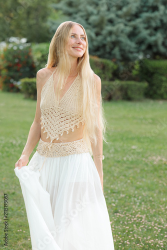 Fotografía A young woman with long blonde hair stands smiling in a white flowing skirt in a