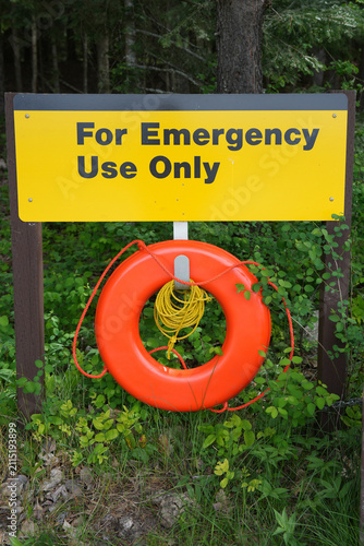 Bright orange life ring with coiled yellow rope hangs beneath a yellow sign reading 