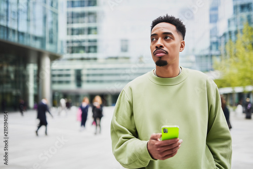Thoughtful young black man holding smartphone in modern urban corporate city square