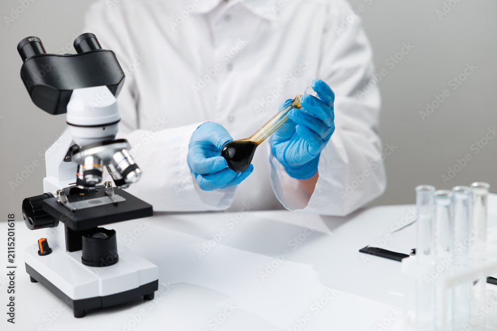 Fototapeta premium Laboratory oil analysis with technician holding dark oil sample for viscosity testing and research background for report design
