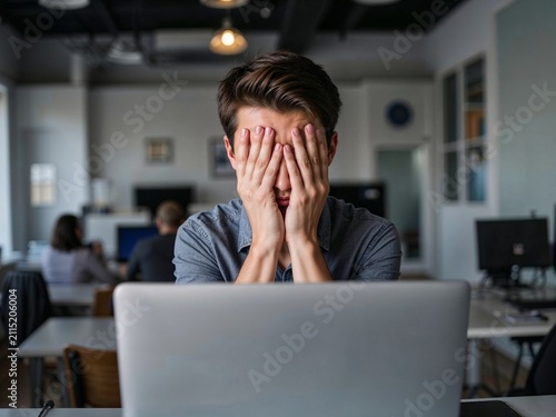 Young man feeling stressed while working on laptop in office  