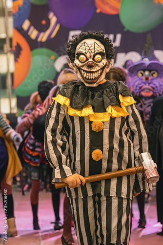Obraz na plátně Participant wearing a striped clown costume and mask poses with toy hammer during Halloween costume contest