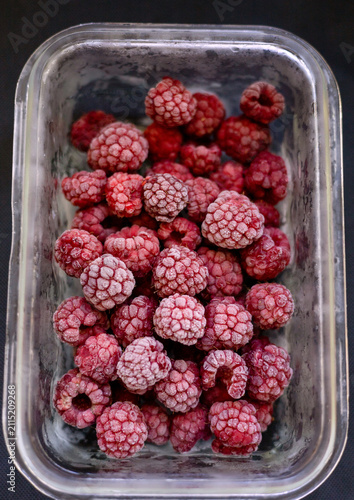 Close-up of frozen raspberries from the garden in a glass container. Frost on the berries. Stored in a refrigerator.