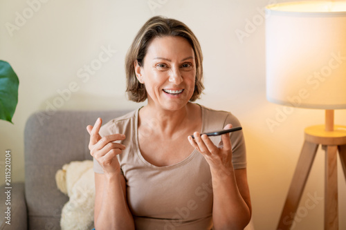 Konstfotografi Laughing middle aged woman dictating voice message to phone