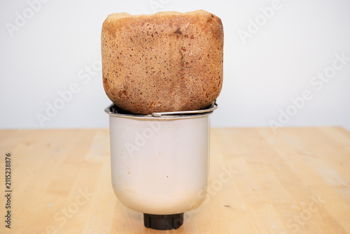 Freshly baked bread loaf cooling on metallic breadmaker container pan standing on wooden table bright modern kitchen interior rustic homemade healthy organic culinary baking concept