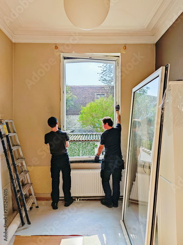 Builders dismantle a window frame in a room together on a spring day.