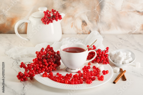 Cup and teapot of hot viburnum tea with cinnamon sticks on color background