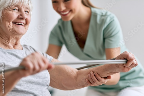 Occupational therapist helps elderly patient with hand resistance bands in warm healthcare setting