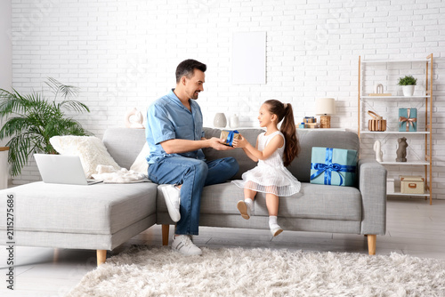 Little daughter giving father present in living room. Fathers Day celebration