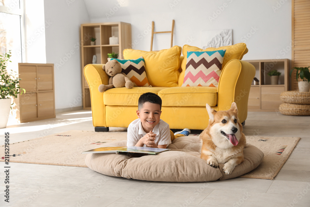 Fototapeta premium Little happy Asian boy reading book with cute Corgi dog at home