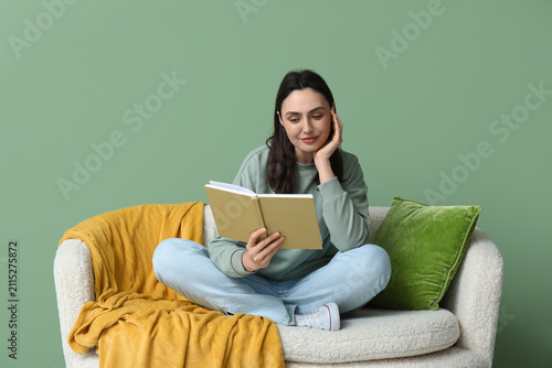 Young woman reading book on sofa in green living room