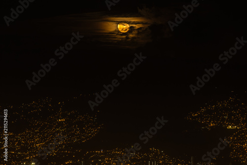 Golden Full Moon Rising Over Medellín City Lights Through Clouds