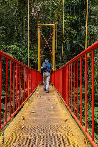Senior Man Walking Across Red and Yellow Suspension Bridge