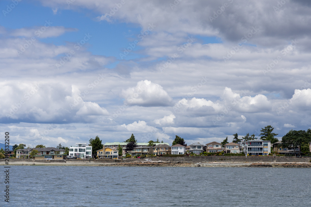 Naklejka premium Waterfront Homes Along Sidney Shoreline Under Dramatic Cloudy Sky on Vancouver Island, BC, Canada