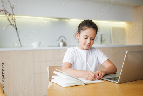 Fotografie Child happily studies at a cozy kitchen table with a laptop and notebook during