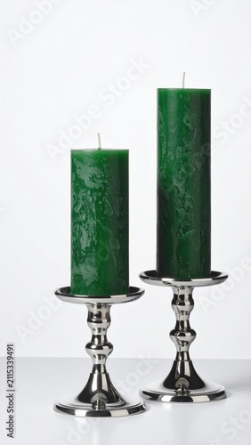 Two tall, dark green cylindrical candles stand in elegant silver candleholders