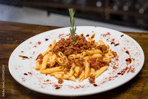 Konstfotografi Penne bolognese pasta topped with minced meat ragu, fresh rosemary sprig, and pa