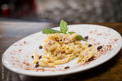Canvastavla Creamy penne pasta with ham, garnished with fresh basil leaves, raisins, and pap