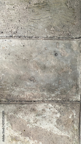 Weathered concrete wall with square tile pattern, showing rough cement texture, stains, and natural aging. Ideal as an architectural background or industrial texture.