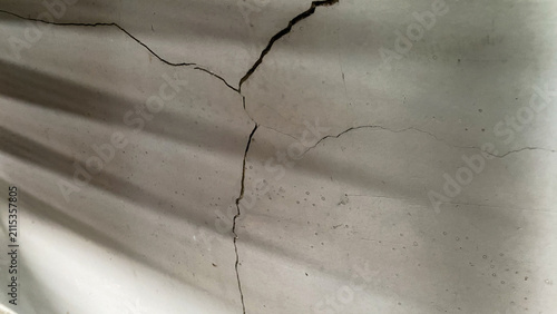 Gray plaster wall with visible cracks and shadow patterns, illustrating structural aging and surface deterioration.