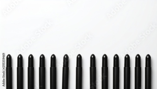 Row of black cosmetic pencils lined up on a white surface
