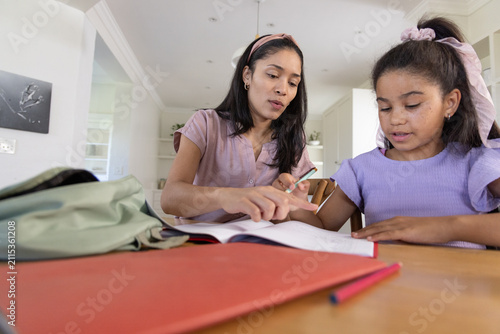 African American mother and child working on homework at home kitchen table with open notebook, pen