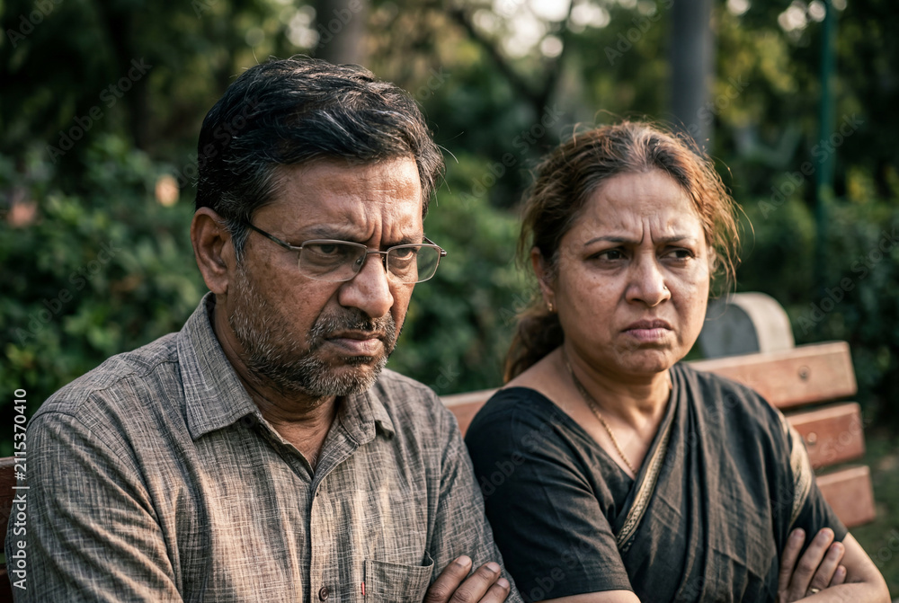 Fototapeta premium Serious senior indian couple sitting together on park bench