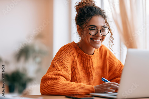Happy young woman using laptop sitting at desk writing notes while watching webinar, studying online, looking at pc screen learning web classes or having virtual call meeting remote working from home.