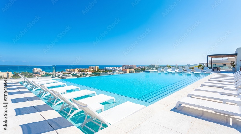 Fototapeta premium Luxury infinity swimming pool overlooking the blue ocean and coastal city skyline