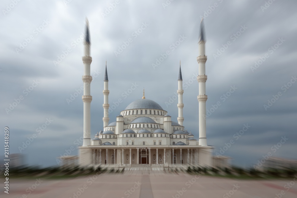 Naklejka premium Grand mosque with tall minarets and domes under cloudy sky.