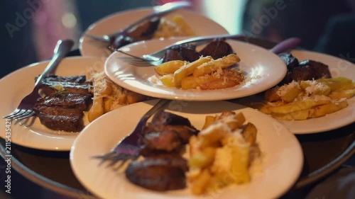 Waiter Carrying Multiple Plates of Beef Steak and Fried Potatoes in Restaurant